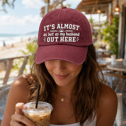 Woman at a beach cafe wearing a maroon washed baseball cap with white embroidered funny husband text