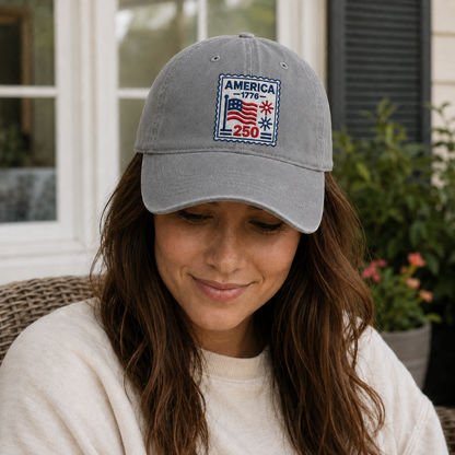 Woman looking down while wearing a grey washed baseball cap with an embroidered patriotic America 250 stamp design