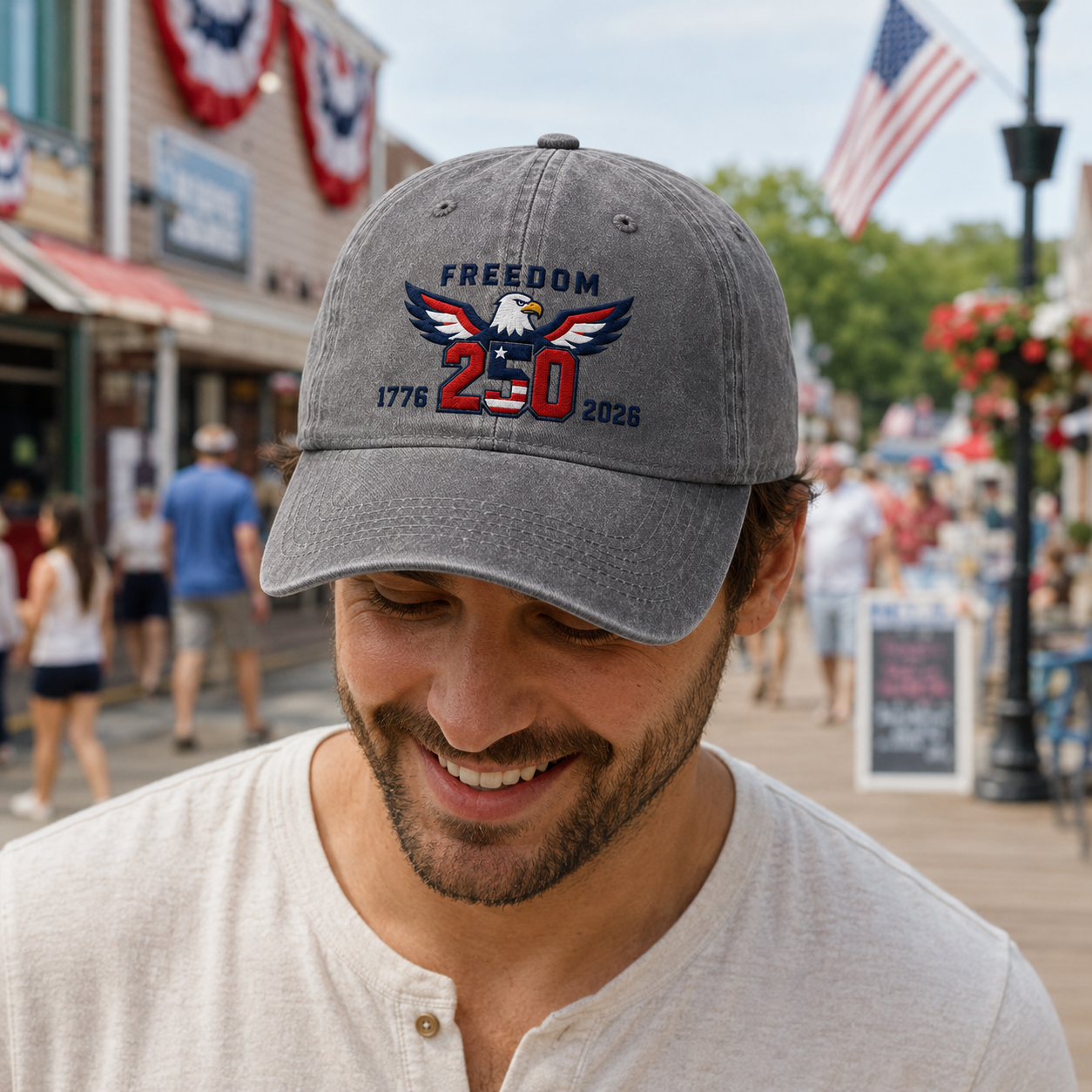 Man smiling on a festive town street wearing a grey washed baseball cap with embroidered patriotic freedom 250 eagle design