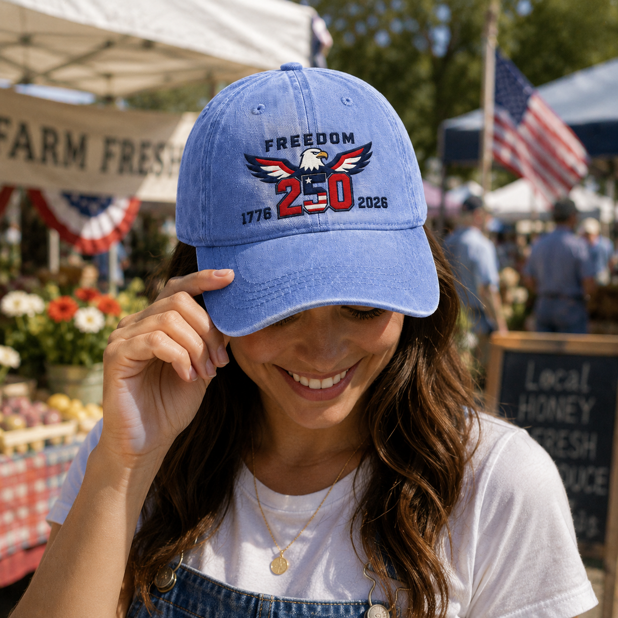Woman smiling at an outdoor farmer's market wearing a light blue washed baseball cap with embroidered patriotic freedom 250 eagle design