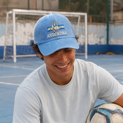 Man holding a football on a blue sports court wearing a light blue washed baseball cap with an embroidered Argentina soccer goose design