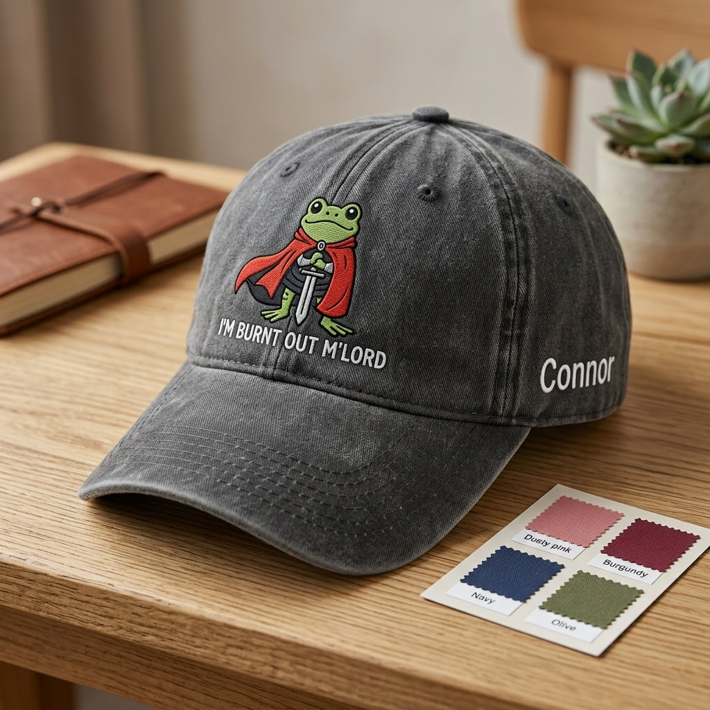 Gray cap with a frog graphic and text on a wooden surface, next to a color swatch card.