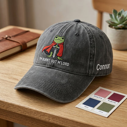 Gray cap with a frog graphic and text on a wooden surface, next to a color swatch card.