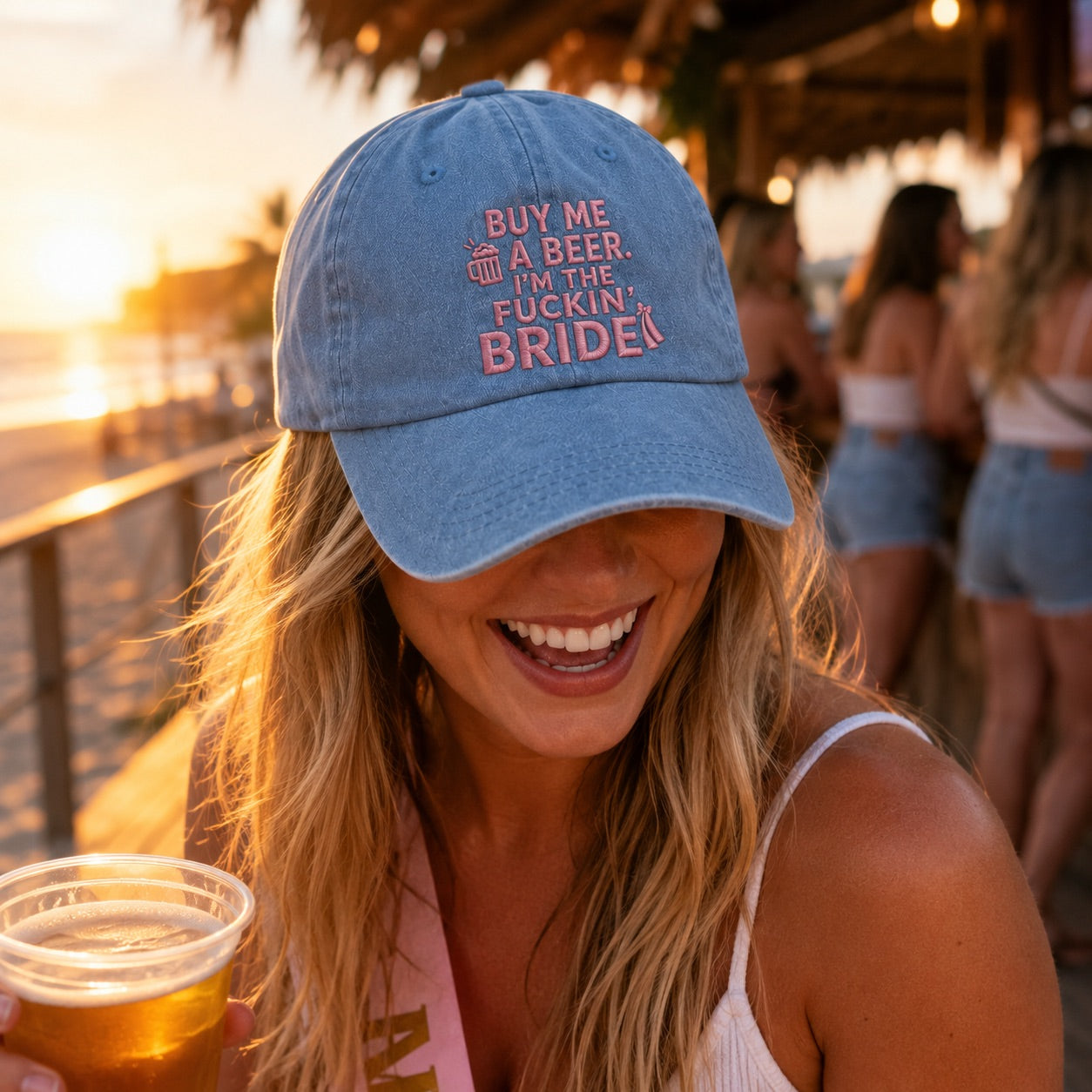 Woman wearing a blue cap with text, holding a drink, at a beachside bar.
