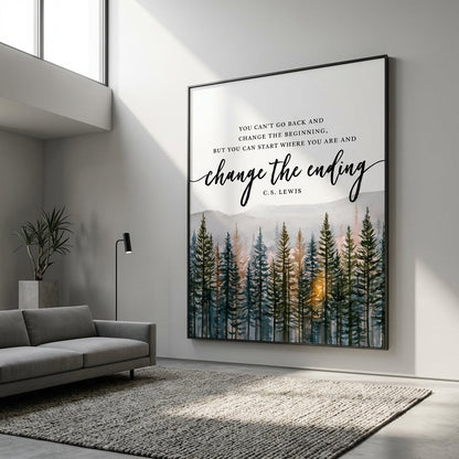 A framed wall art print hanging on a light gray wall in a modern living room. The print features a forest scene with tall dark trees and a warm glowing sun near the horizon, with the quote 'YOU CAN'T GO BACK AND CHANGE THE BEGINNING, BUT YOU CAN START WHERE YOU ARE AND change the ending' and 'C.