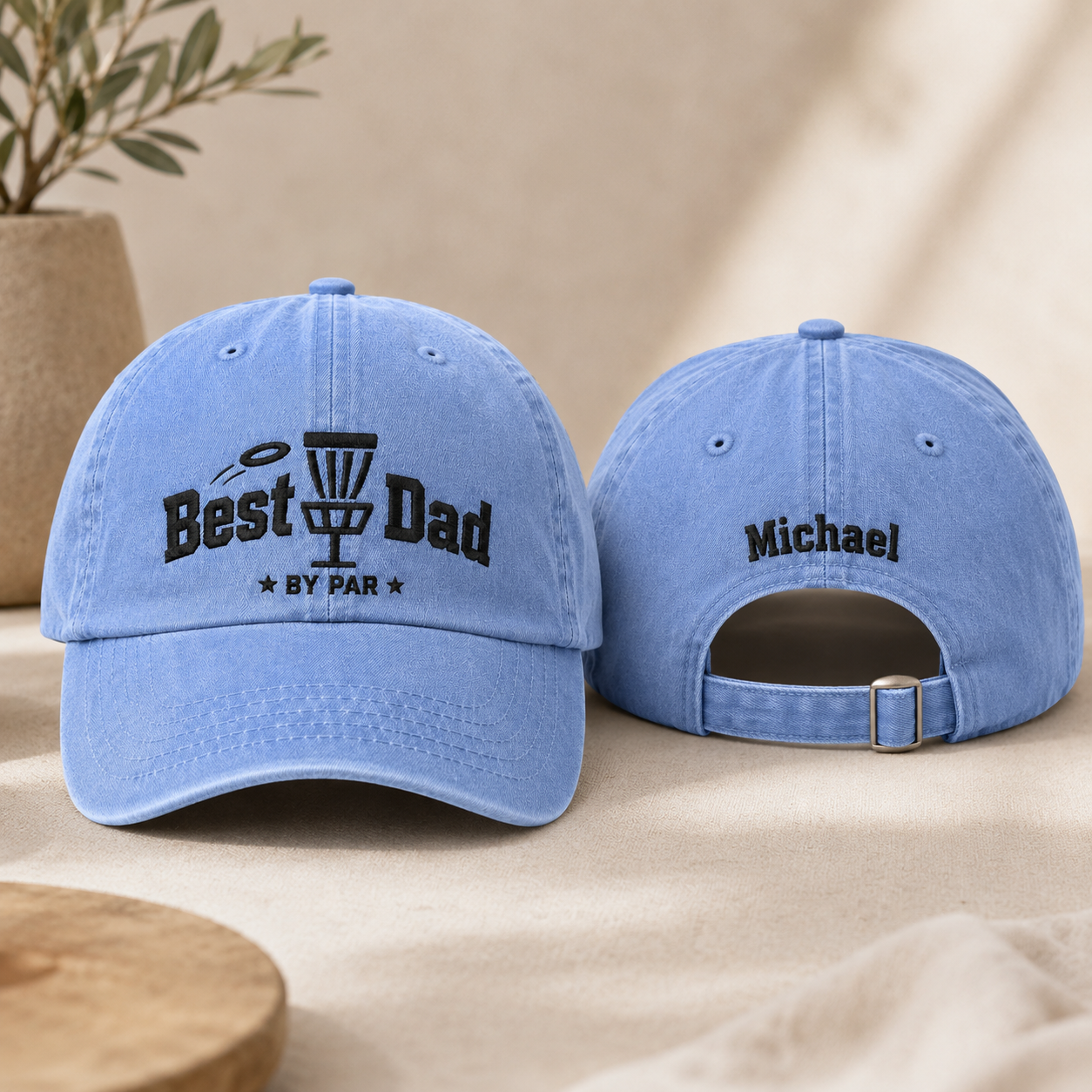 Front and back view of a light blue washed baseball cap with black embroidered disc golf best dad by par design and custom name text