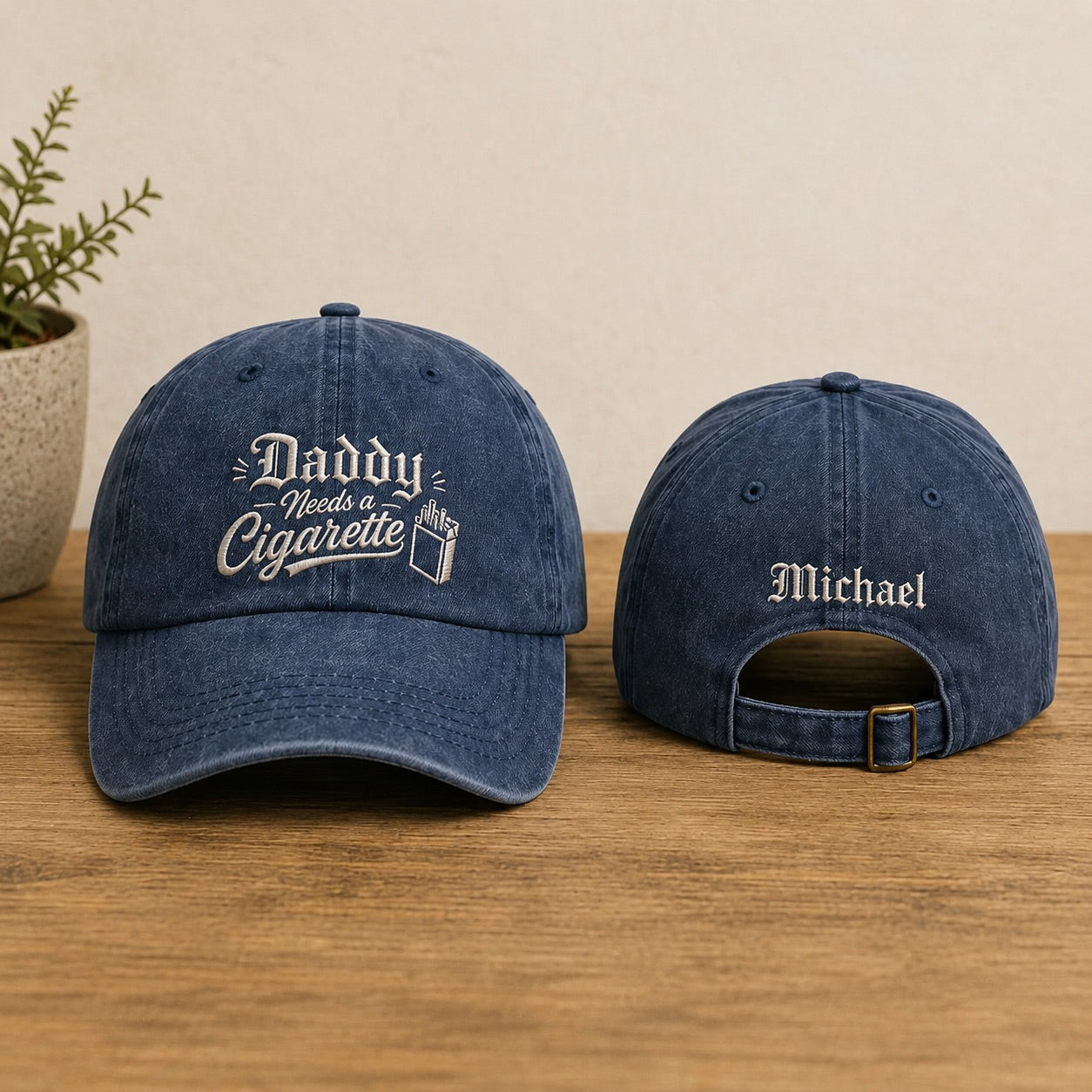 Two blue denim baseball caps with embroidered text on a wooden surface.
