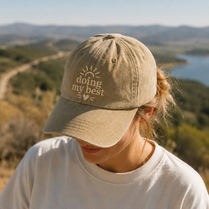 Person wearing a cap with 'doing my best' text in a scenic outdoor setting
