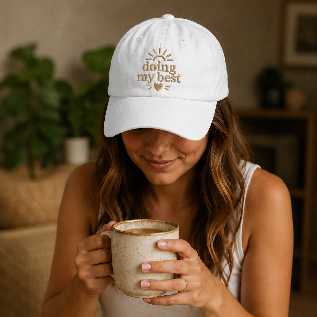 Woman wearing a white cap with 'doing my best' text, holding a mug indoors.