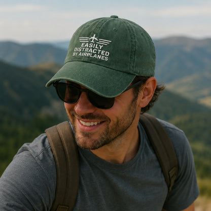 Man wearing a green cap with text and sunglasses, standing against a mountainous landscape.