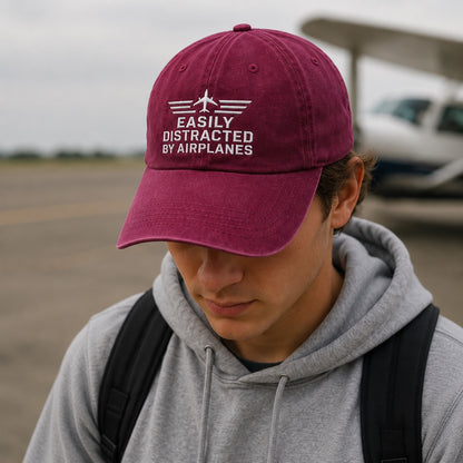 Person wearing a maroon cap with text, standing in an outdoor setting.