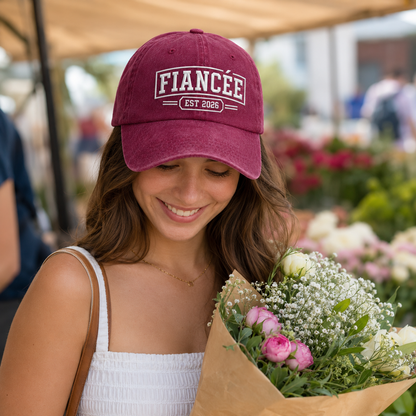 Woman holding a flower bouquet while wearing a maroon washed baseball cap with embroidered fiancee design
