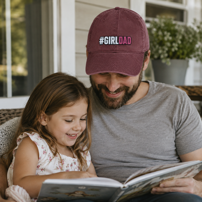Father and daughter reading a book together while he wears a maroon washed baseball cap with embroidered girl dad text