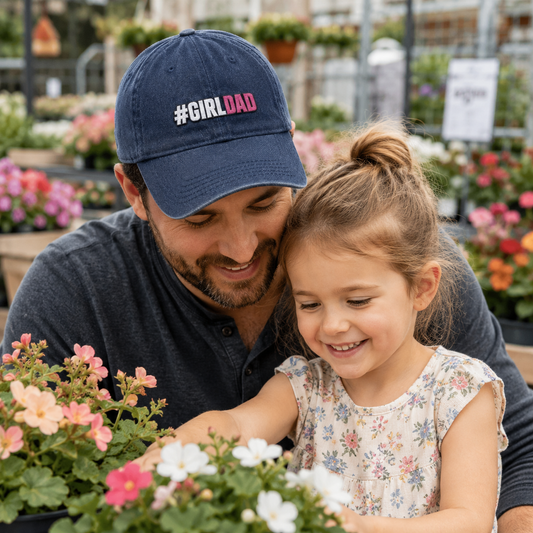 Father and daughter looking at plants in a greenhouse while he wears a navy washed baseball cap with embroidered girl dad text