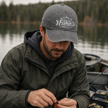 Man preparing tackle while on a fishing boat wearing a grey washed baseball cap with white embroidered Fishin mountain design