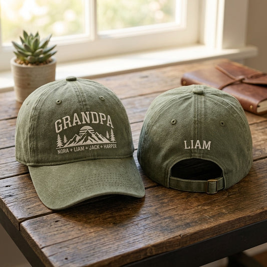 Two green baseball caps on a wooden surface with 'GRANDPA' and names printed on them.