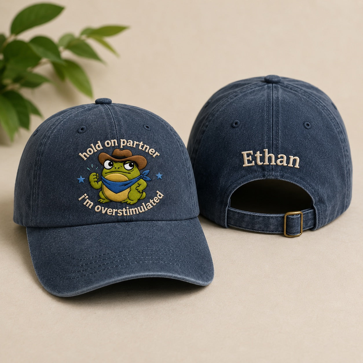 Two blue baseball caps with a cartoon frog design and text on a beige background.