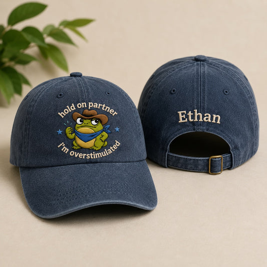 Two blue baseball caps with a cartoon frog design and text on a beige background.
