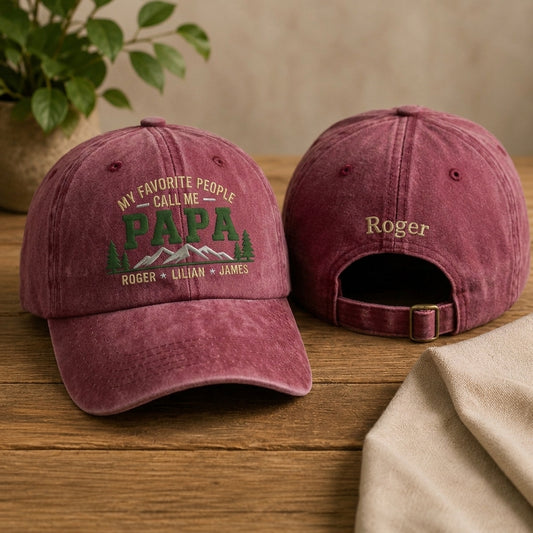 Two gray baseball caps with embroidered text on a wooden surface.