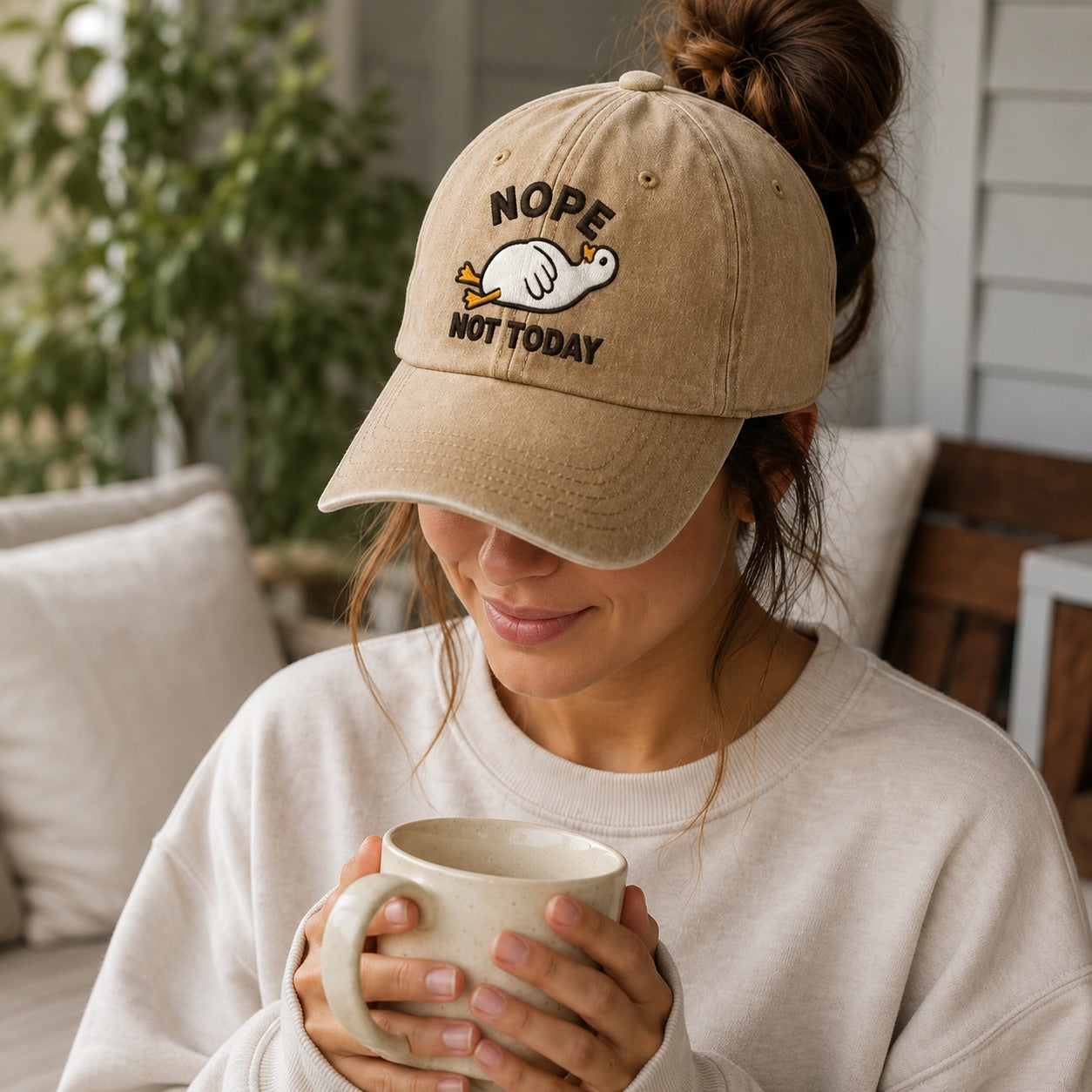 Woman wearing a beige cap with 'NOPE NOT TODAY' text and holding a mug indoors.