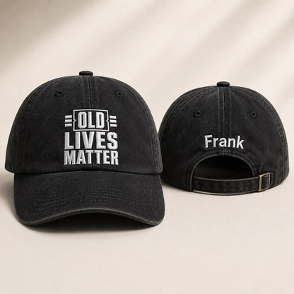 Black baseball cap with 'Old Lives Matter' front and 'Frank' back on beige background