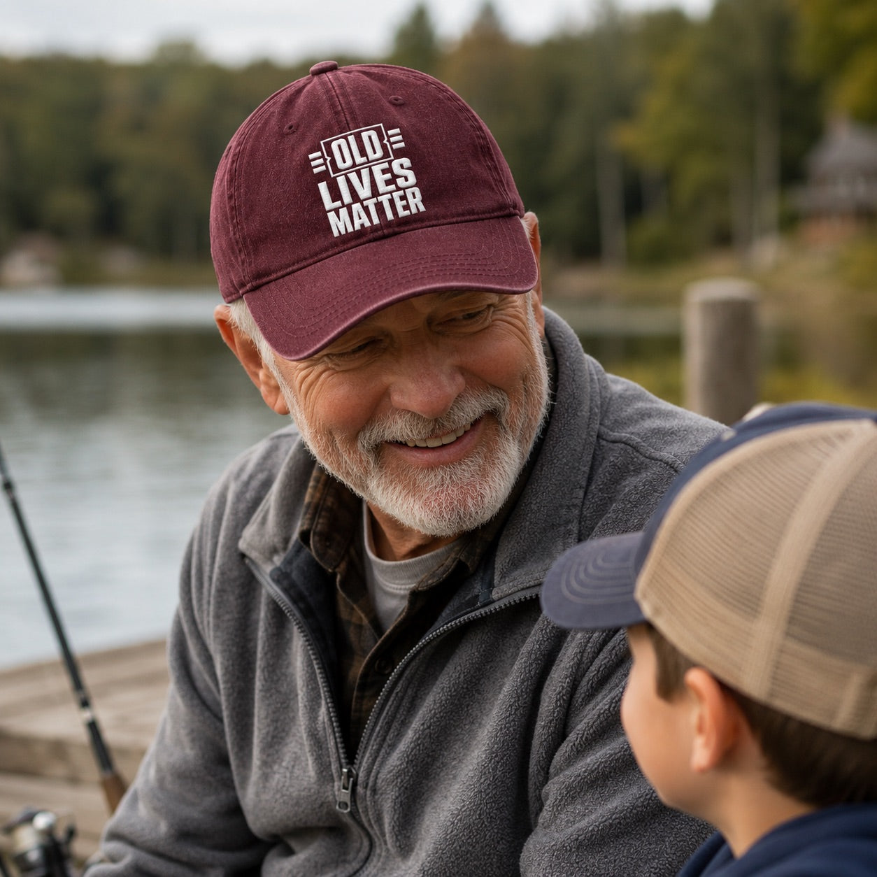 Man wearing a cap with 'Old Lives Matter' text, sitting by a lake with a child.