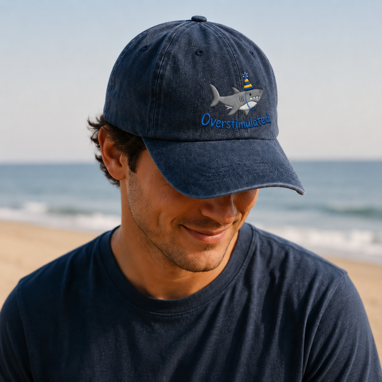 Man wearing a navy blue cap with a shark design and 'Overshuffled' text on a beach.