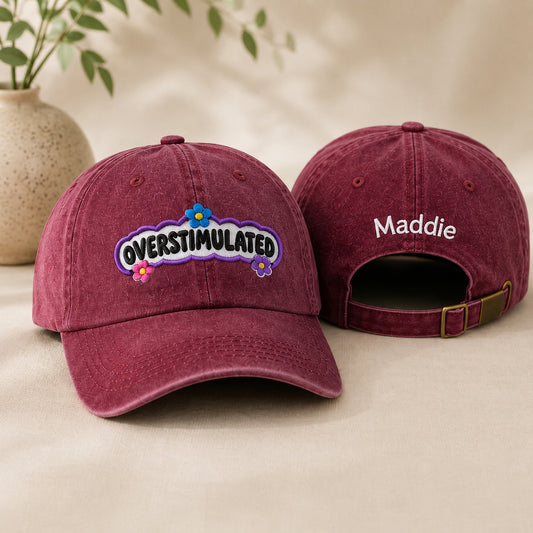 Two maroon baseball caps with 'Overstimulated' and 'Maddie' text on a beige surface.