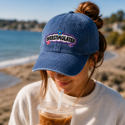 Person wearing a blue cap with 'OVERSTIMULATED' text at the beach