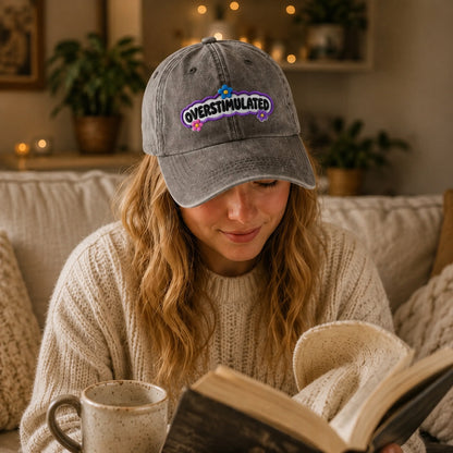 Woman reading a book and holding a mug, wearing an 'Overstimulated' cap in a cozy indoor setting.