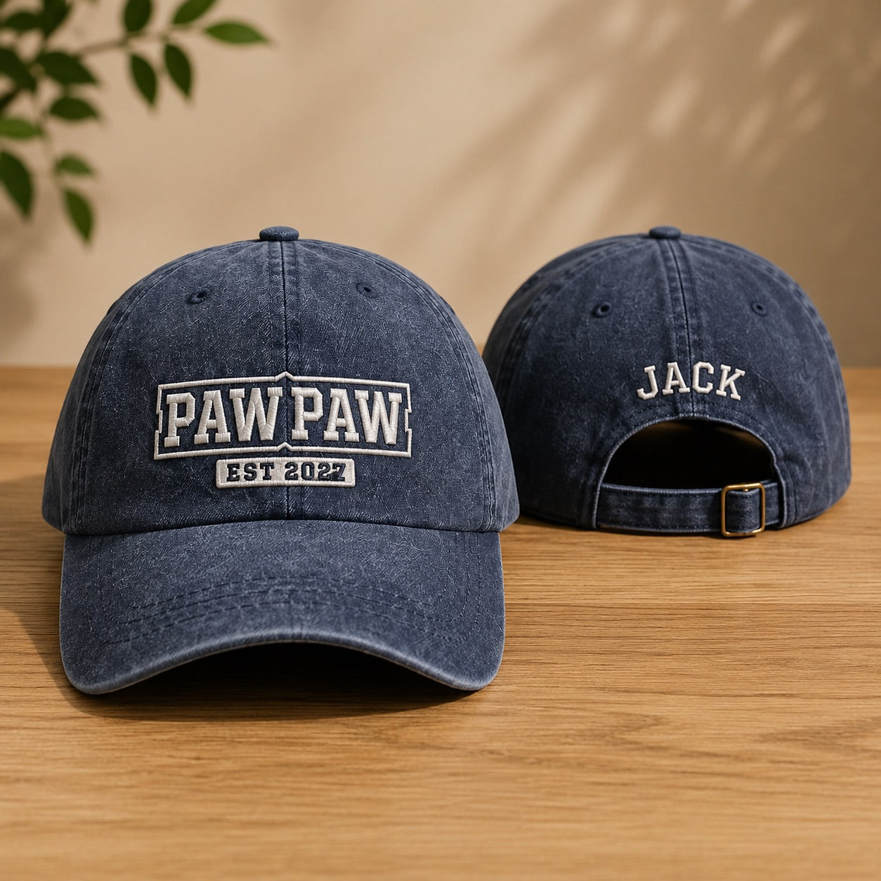 Two navy blue baseball caps with 'PAW PAW EST 2022' and 'JACK' text on a wooden surface.