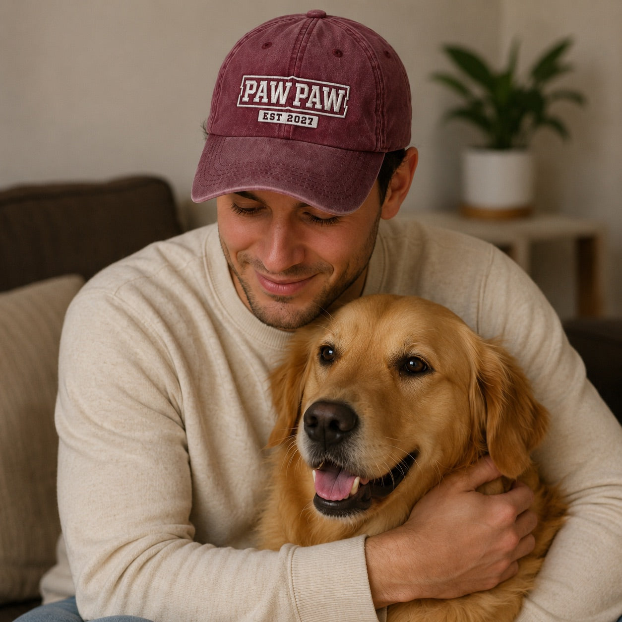Man wearing a maroon 'PAW PAW' cap sitting with a golden dog indoors.