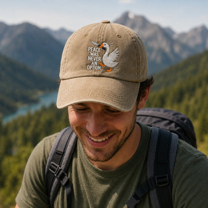 Man wearing a cap with a goose design and text, standing in a mountainous landscape.