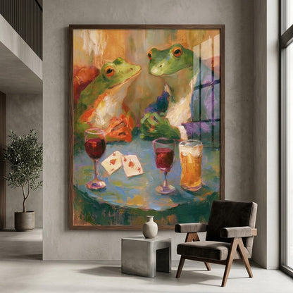 A framed vertical canvas print depicting two green frogs at a table with wine and beer glasses, displayed on a gray wall in a modern living room setting.
