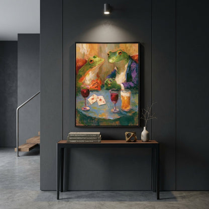 A framed colorful painting of two green frogs sitting at a table with drinks and playing cards, displayed on a dark gray paneled wall above a console table in a modern interior setting.
