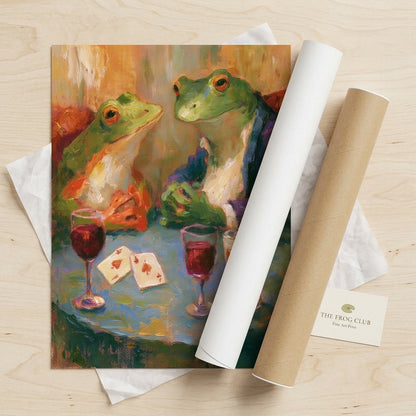 A rolled art print and matching cardboard mailing tube on a light wood surface. The print shows an impressionistic painting of two frogs seated at a table with glasses of red wine and playing cards.