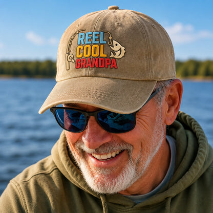 Man wearing a cap with 'Reel Cool Grandpa' text by a body of water.