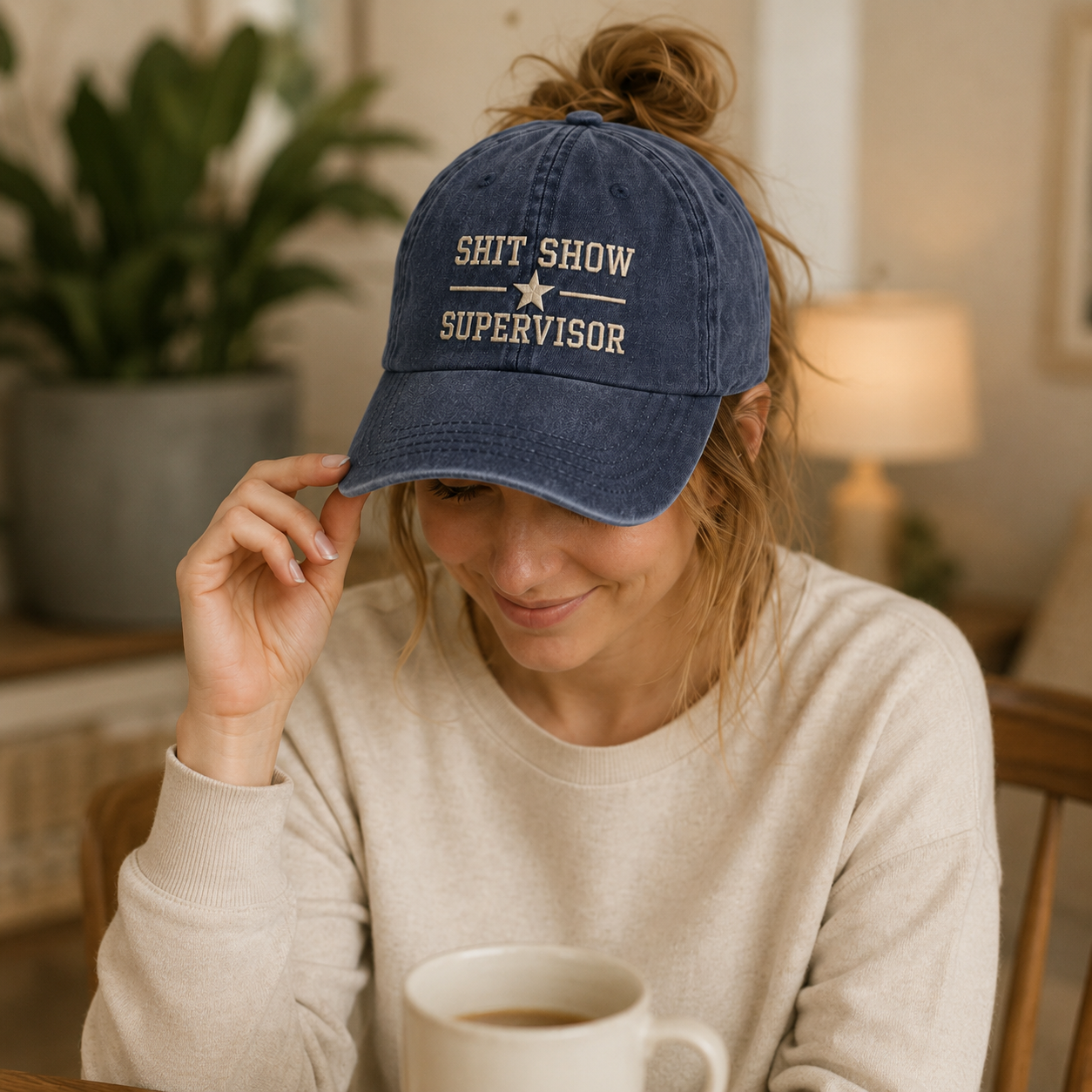 Person wearing a blue cap with text, sitting indoors holding a mug.