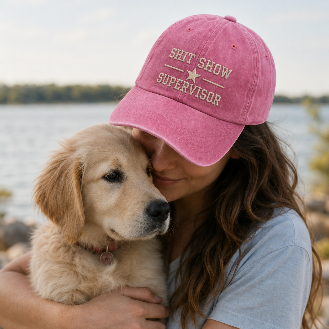 Person wearing a pink cap with text holding a puppy by a lake