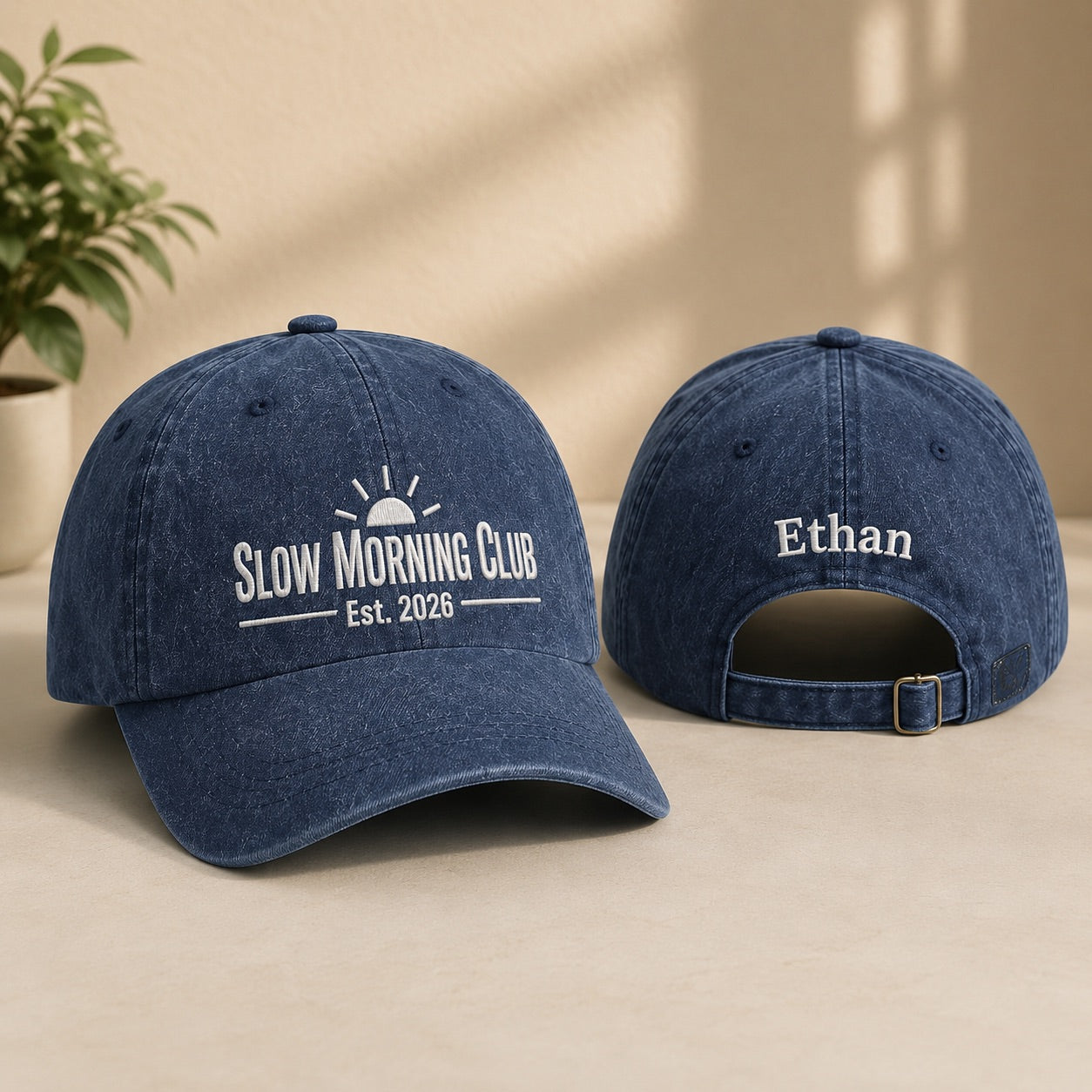 Two blue baseball caps with 'Slow Morning Club' and 'Ethan' text on a beige surface.