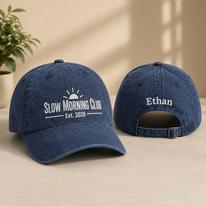 Two blue baseball caps with 'Slow Morning Club' and 'Ethan' text on a beige surface.
