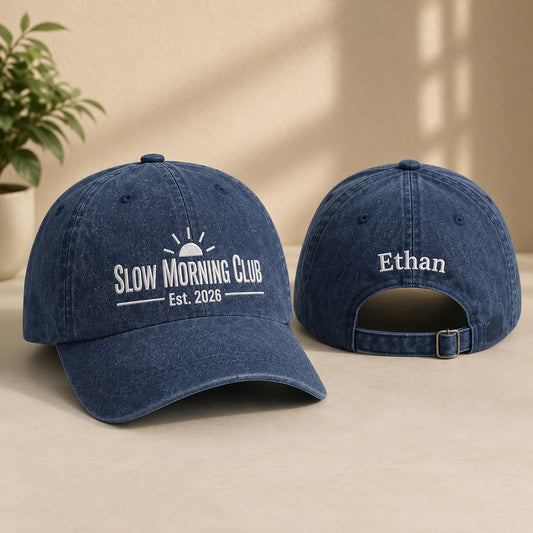 Two blue baseball caps with 'Slow Morning Club' and 'Ethan' text on a beige surface.