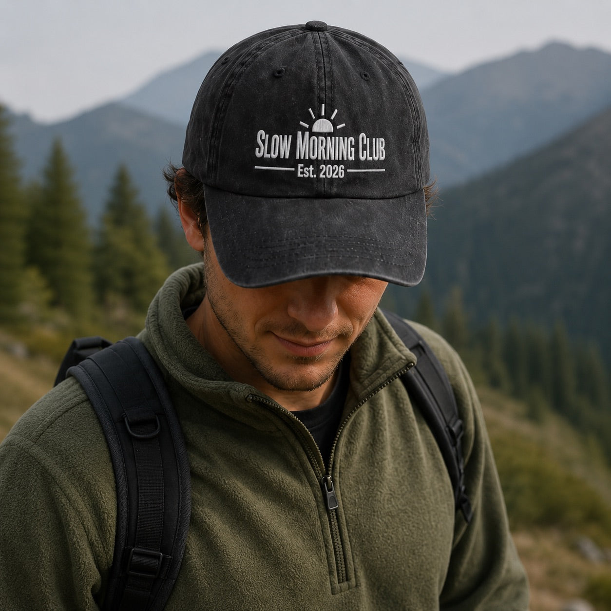 Man wearing a 'Slow Morning Club' cap in a mountainous landscape