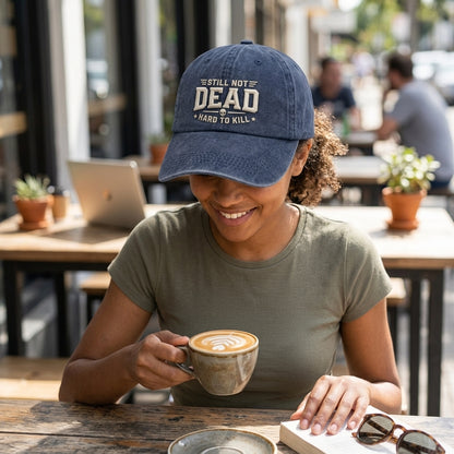 Person wearing a cap with text, holding a coffee cup in an outdoor cafe setting
