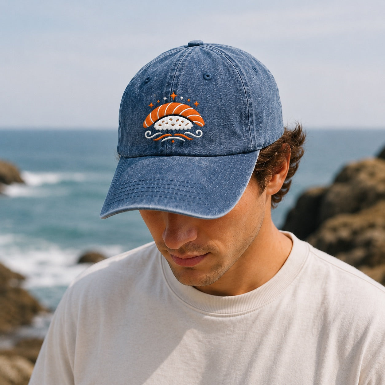 Man wearing a denim cap with a sushi design by the ocean