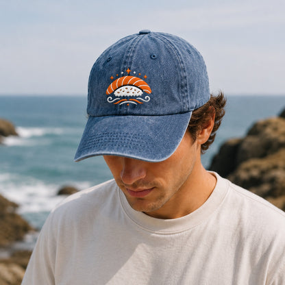 Man wearing a denim cap with a sushi design by the ocean