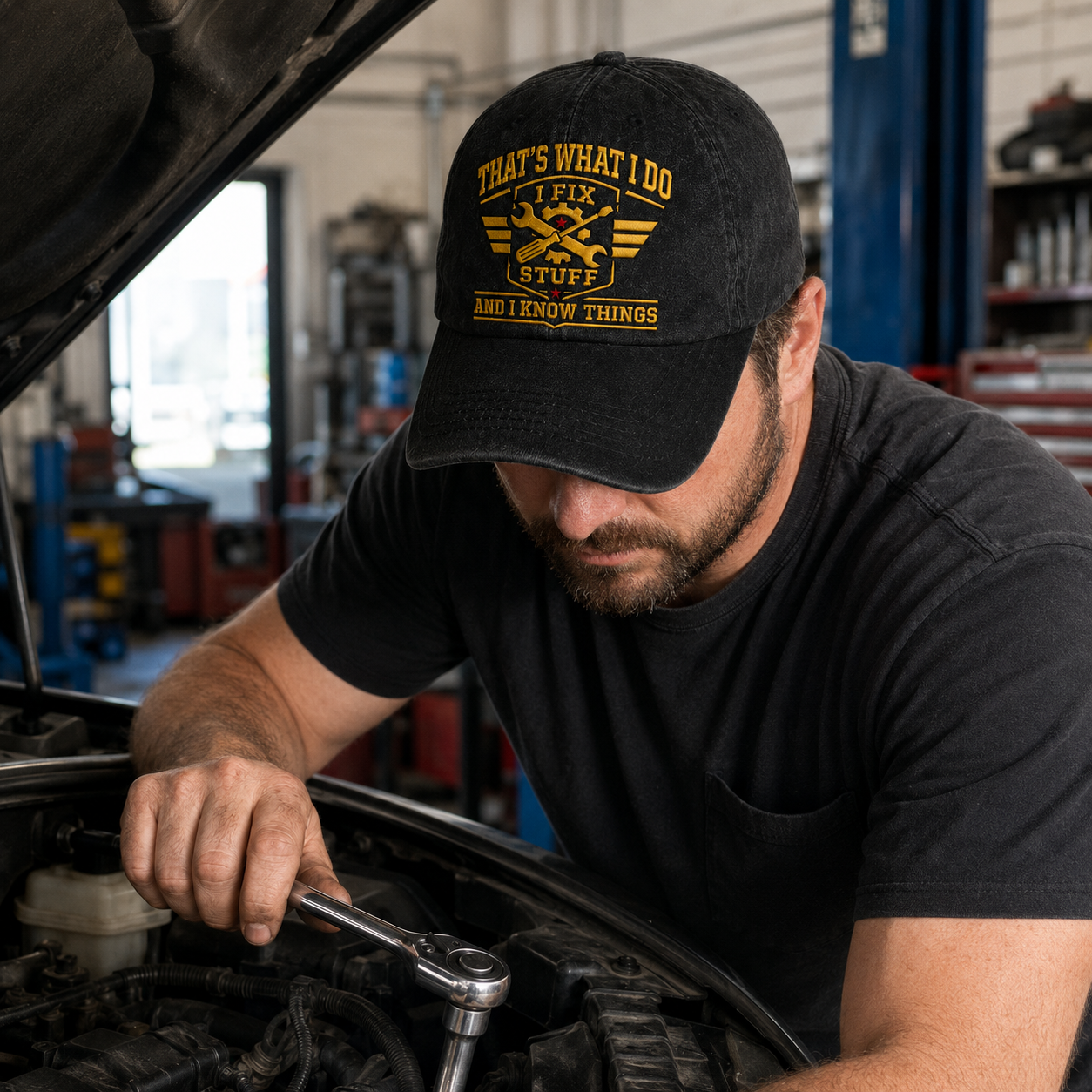 Black washed cotton baseball cap with yellow embroidered mechanic design worn by a man fixing a car engine.