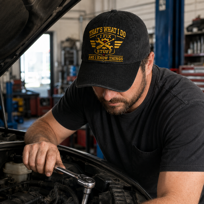 Black washed cotton baseball cap with yellow embroidered mechanic design worn by a man fixing a car engine.