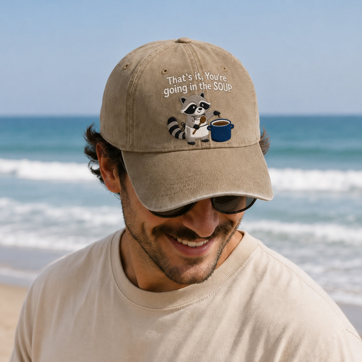 Man wearing a cap with a raccoon graphic and text at the beach