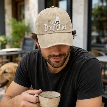 Sand washed cotton baseball cap with embroidered The Dogfather logo worn by a man drinking coffee.